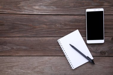 Gri ahşap arka plan üstünde defter ile akıllı telefon. Smartphone ile siyah ekran