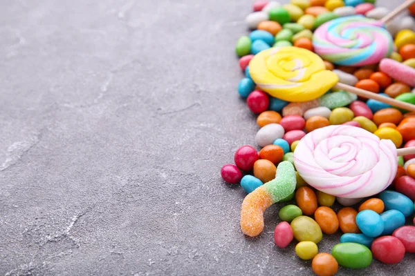 Colorful lollipop and different colored round candy on grey concrete backgrond