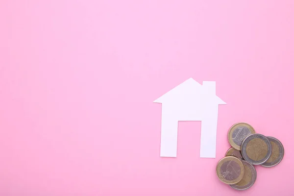 Casa de papel blanco con monedas sobre fondo rosa — Foto de Stock