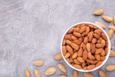 Gri ahşap arka planda beyaz bir kase badem.