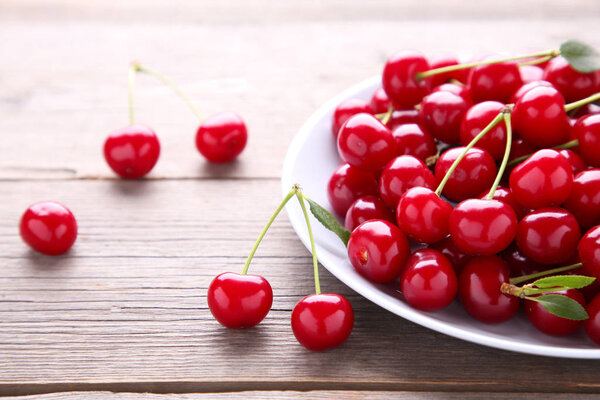 Fresh red cherry fruit in plate on grey wooden table