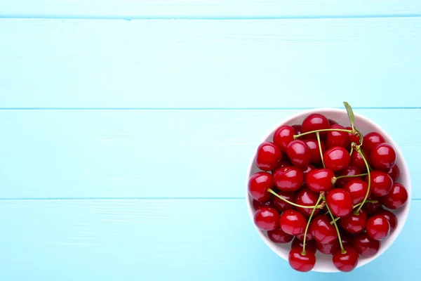 Fresh red cherry fruit in plate on blue wooden table — Stock Photo, Image