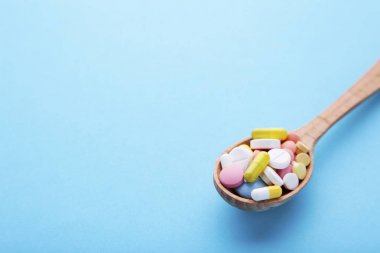 Çeşitli ilaç tıp hap, tablet ve kapsül üzerinde mavi zemin üzerine tahta kaşık