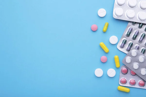 Kolorowe pigułki i tabletki w blistrze na niebieskim tle, widok z góry — Zdjęcie stockowe