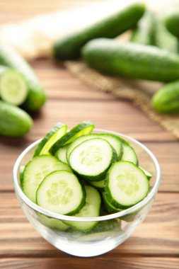 Kahverengi ahşap arka planda, kâsede taze salatalık dilimleri. Üst görünüm