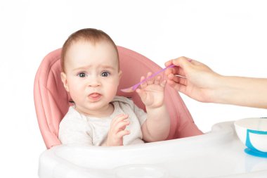 Anne, beyaz arka planda izole edilmiş sandalyedeki tatlı bebeğini besliyor. Üst görünüm