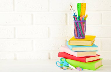 Beyaz tuğlalı arka planda çok renkli okul kitapları ve kırtasiye malzemeleri. Boşluğu kopyala