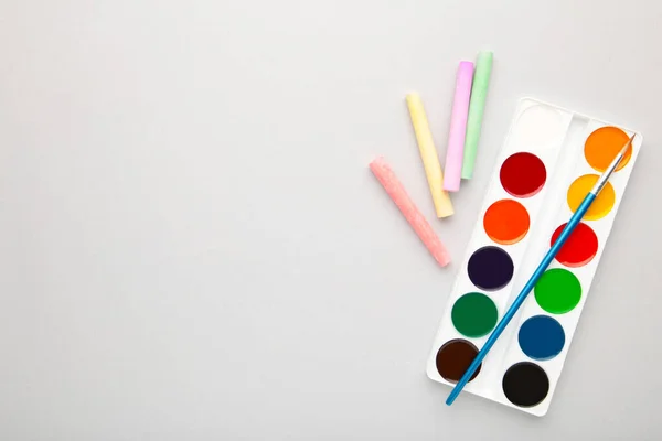 Watercolor paints set with brushes and crayons for drawing on grey background. Top view