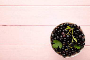 Pembe ahşap arka planda beyaz bir kasede siyah frenk üzümü. Üst görünüm