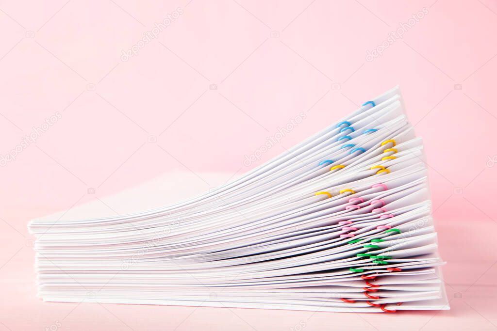 Colorful paper clip with pile of overload white paperwork on pink. Top view