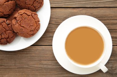 Gri ahşap masada bir fincan kahve ve çikolatalı kurabiye. Üst görünüm