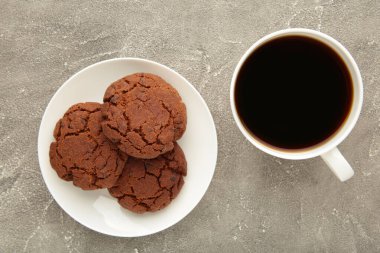 Gri masada bir fincan kahve ve çikolatalı kurabiye. Üst görünüm