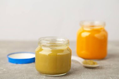 Gri arka planda besin değeri olan cam kavanozlar. Kaşıklı sebze püresi..