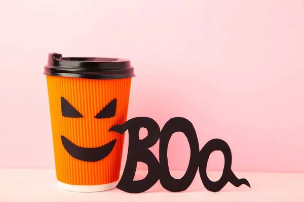 Paper cup with Halloween face in the pink background with inscription boo. Top view