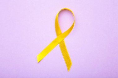 Mor pastel arka planda sarı farkındalık kurdelesi. Üst görünüm
