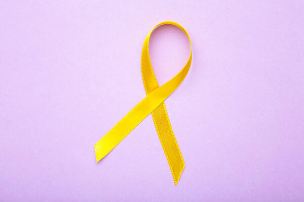 Yellow awareness ribbon on purple pastel background. Top view