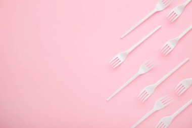 Pembe arka planda bir sürü plastik çatal var. Üst görünüm.