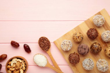 Sağlıklı ev yapımı enerji topları, kızılcık, fındık, tarih ve pembe arka planda kesilmiş yulaf. Mesaj için yer var. Üst görünüm