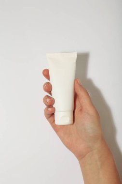 Beyaz arka planda boş beyaz plastik bir tüp tutuyor. Kozmetik güzellik ürünü markalaşma modeli.