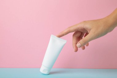 Pembe arka planda boş beyaz plastik bir tüp tutuyor. Kozmetik güzellik ürünü markalaşma modeli.