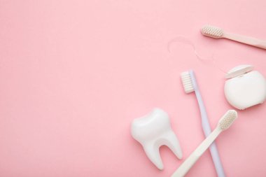 Diş bakımı için sağlıklı dişçi aletleri. Pembe arka planda diş fırçası ve diş ipiyle plastik diş fırçası. Üst görünüm