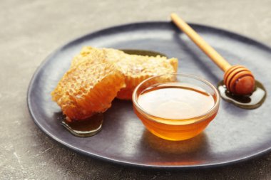 Bir kase tatlı bal, kepçeler ve siyah tabakta taraklar. Üst görünüm