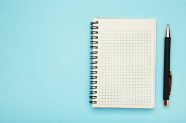 Mavi arka planda not defteri ve pembe kalem. Üst görünüm