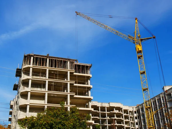 Construction site background. Crane and concrete building against blue sky.