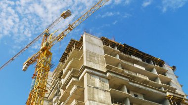 İskele yakınındaki iki büyük vinç. Beton bina inşaat altında. İnşaat alanı.