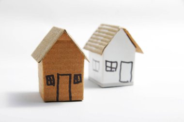 Kahverengi karton ev minyatürü, beyaz izole bir zemin üzerinde, gerekli ve yatırım fikirlerini temsil ediyor.