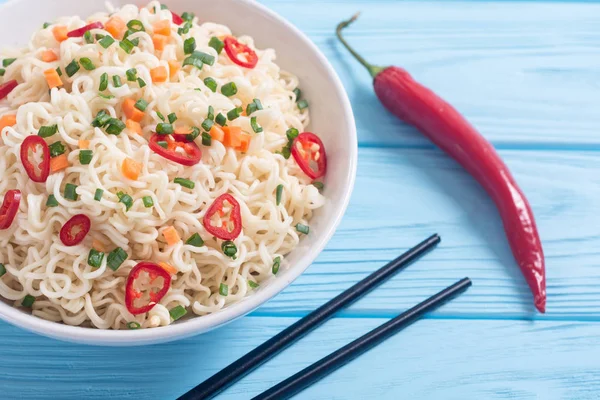 Instant noodles in bowl with chili peppers , onion and carrots