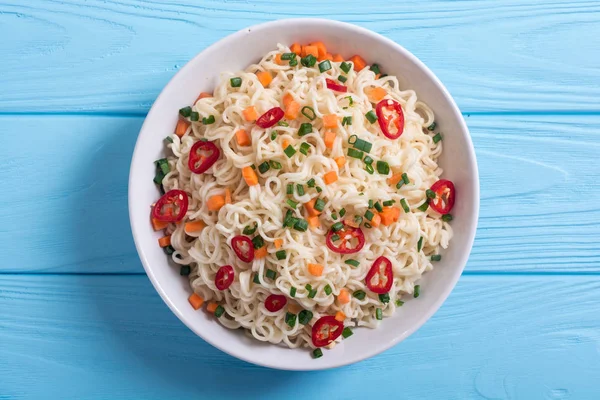 Instant noodles in bowl with chili peppers , onion and carrots