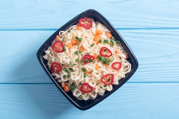 Instant noodles in bowl with chili peppers , onion and carrots