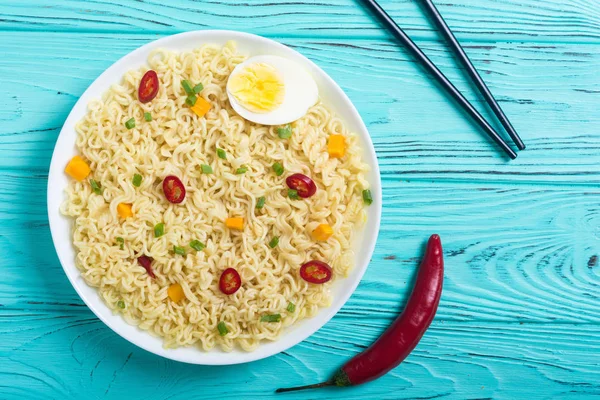 Instant noodles in bowl with chili peppers, eggs , onion and carrots