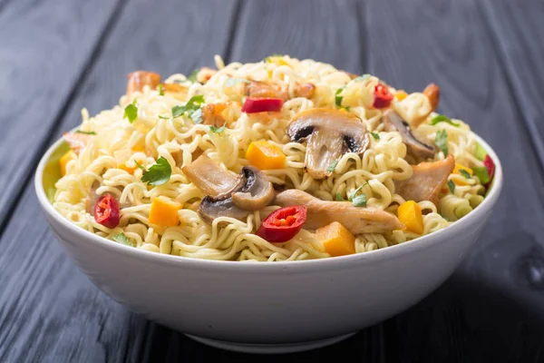 Instant noodles in bowl with chili peppers, mushrooms , chicken and carrots