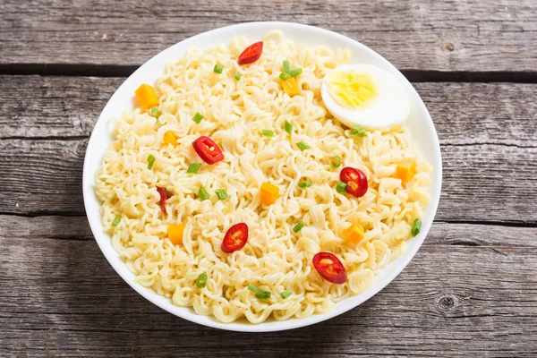 Instant noodles in bowl with chili peppers, eggs , onion and carrots