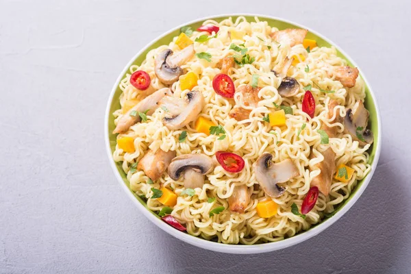 Instant noodles in bowl with chili peppers, mushrooms , chicken and carrots