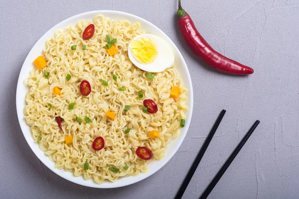 Instant noodles in bowl with chili peppers, eggs , onion and carrots