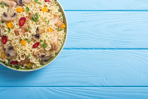 Instant noodles in bowl with chili peppers, mushrooms , chicken and carrots