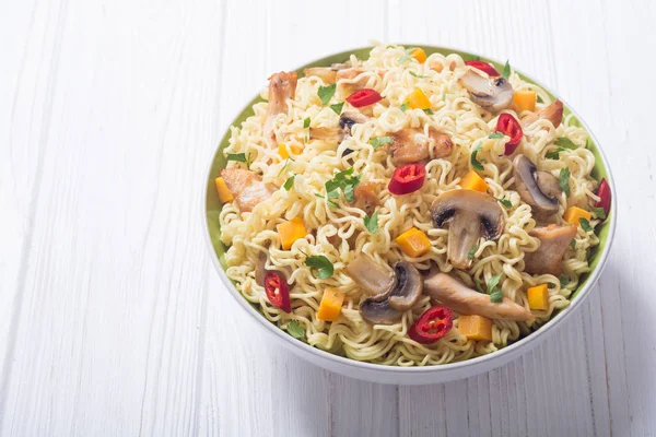 Instant noodles in bowl with chili peppers, mushrooms , chicken and carrots