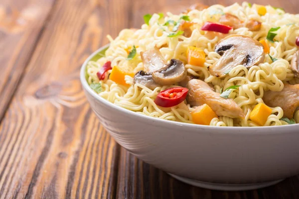 Instant noodles in bowl with chili peppers, mushrooms , chicken and carrots