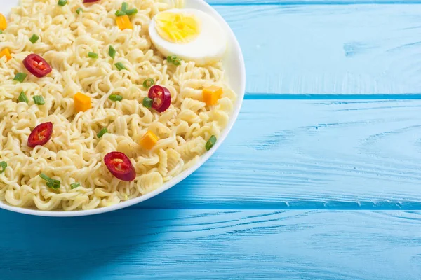 Instant noodles in bowl with chili peppers, eggs , onion and carrots