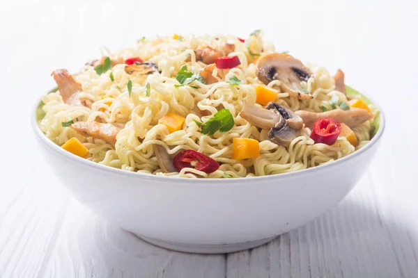 Instant noodles in bowl with chili peppers, mushrooms , chicken and carrots