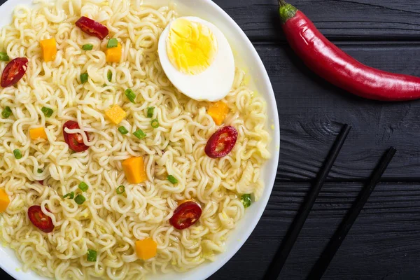 Instant noodles in bowl with chili peppers, eggs , onion and carrots