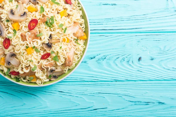 Instant noodles in bowl with chili peppers, mushrooms , chicken and carrots