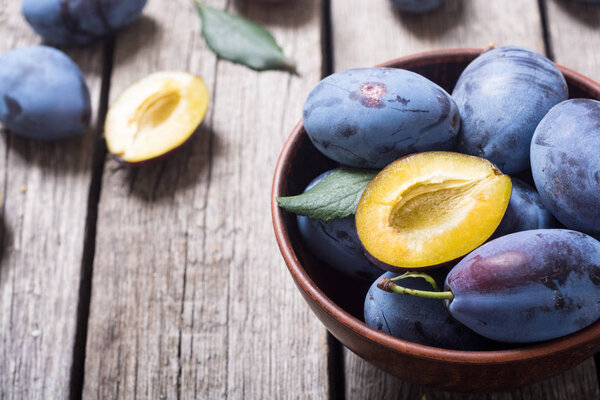 Свежие сливы в миске на деревянном столе. Фруктовый фон
