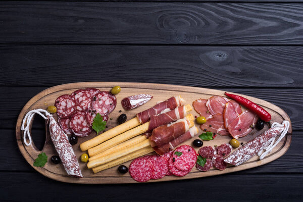 Set of sausages ( ham , salami , jamon ) and olives on wooden board