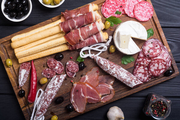 Set of sausages ( ham , salami , jamon ) and olives on wooden board