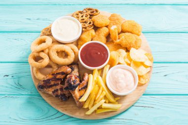 Soğan halkaları, kızarmış kanatlar, patates kızartması ve soslar. Bira tahtası