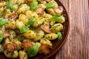 Ahşap arka planda fesleğen, peynir ve mantarlı ev yapımı patates gnocchi.